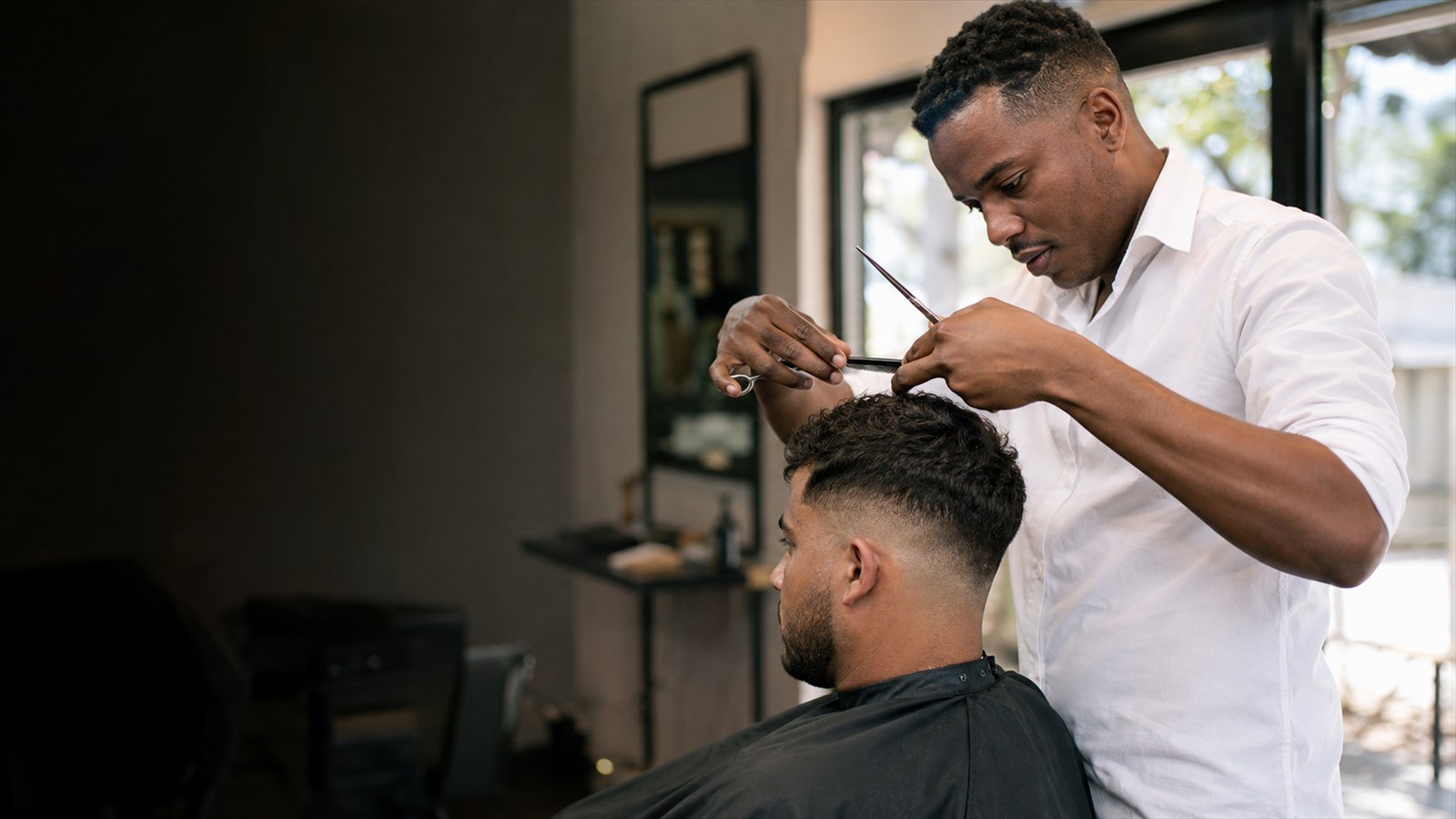 Barber using scissors to shape an adult client's textured fade