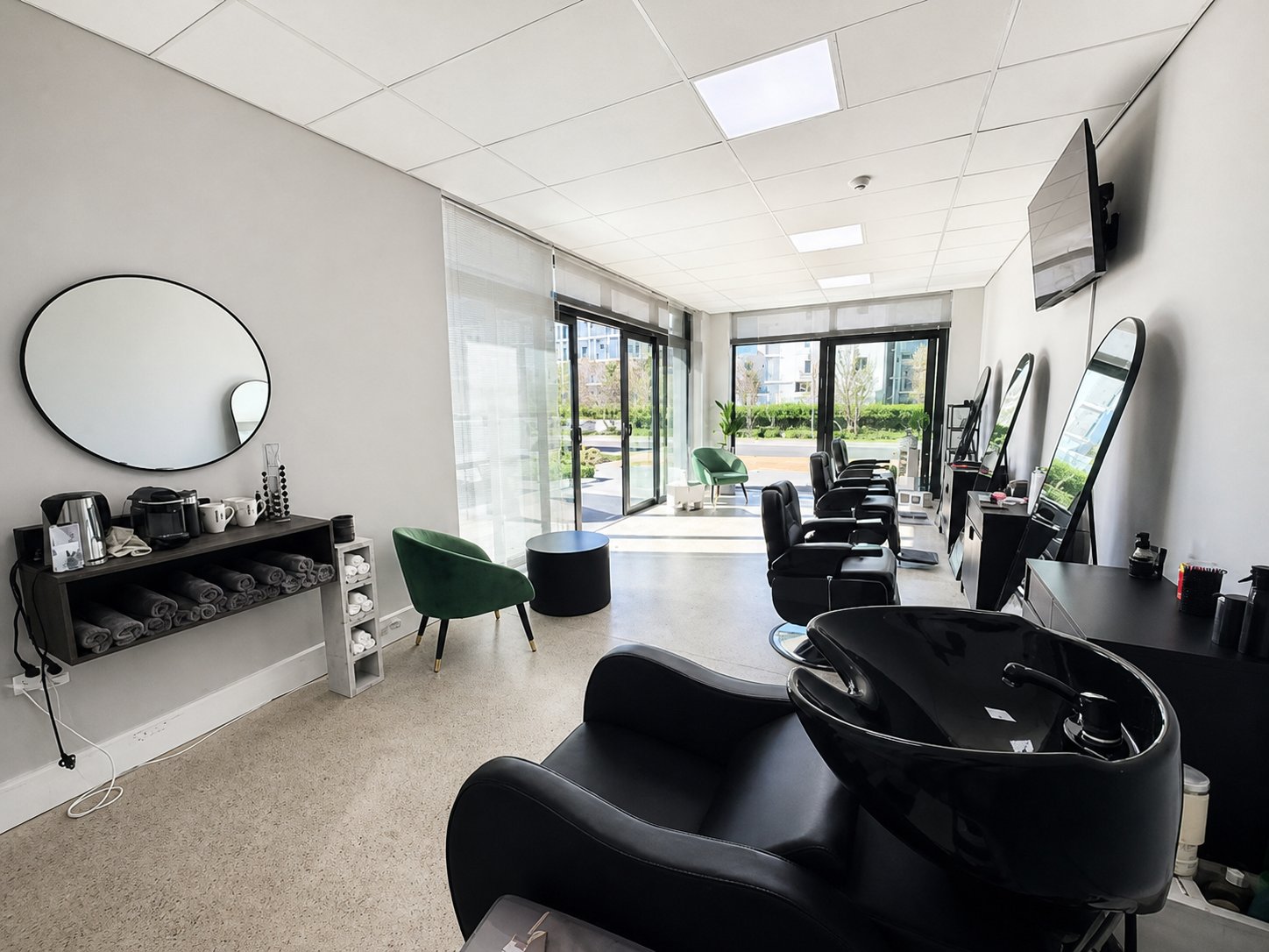 Wide view across the bright shop, wash basin and barber stations